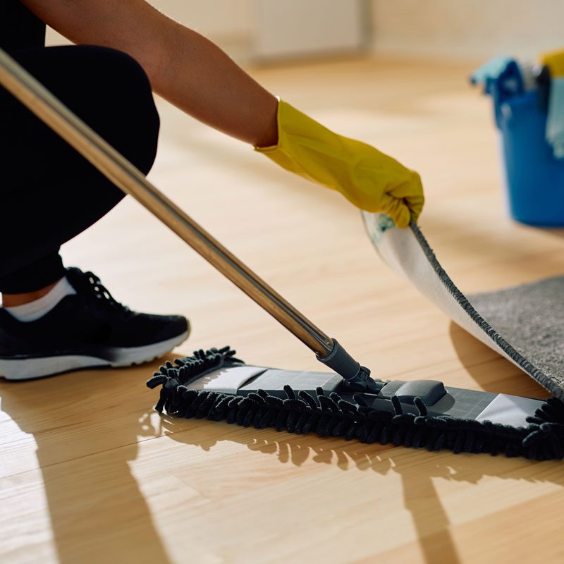 artikelbild Leistungsseite mann putzt boden Eine Person mit gelben Handschuhen reinigt den Boden mit einem Wischmob.