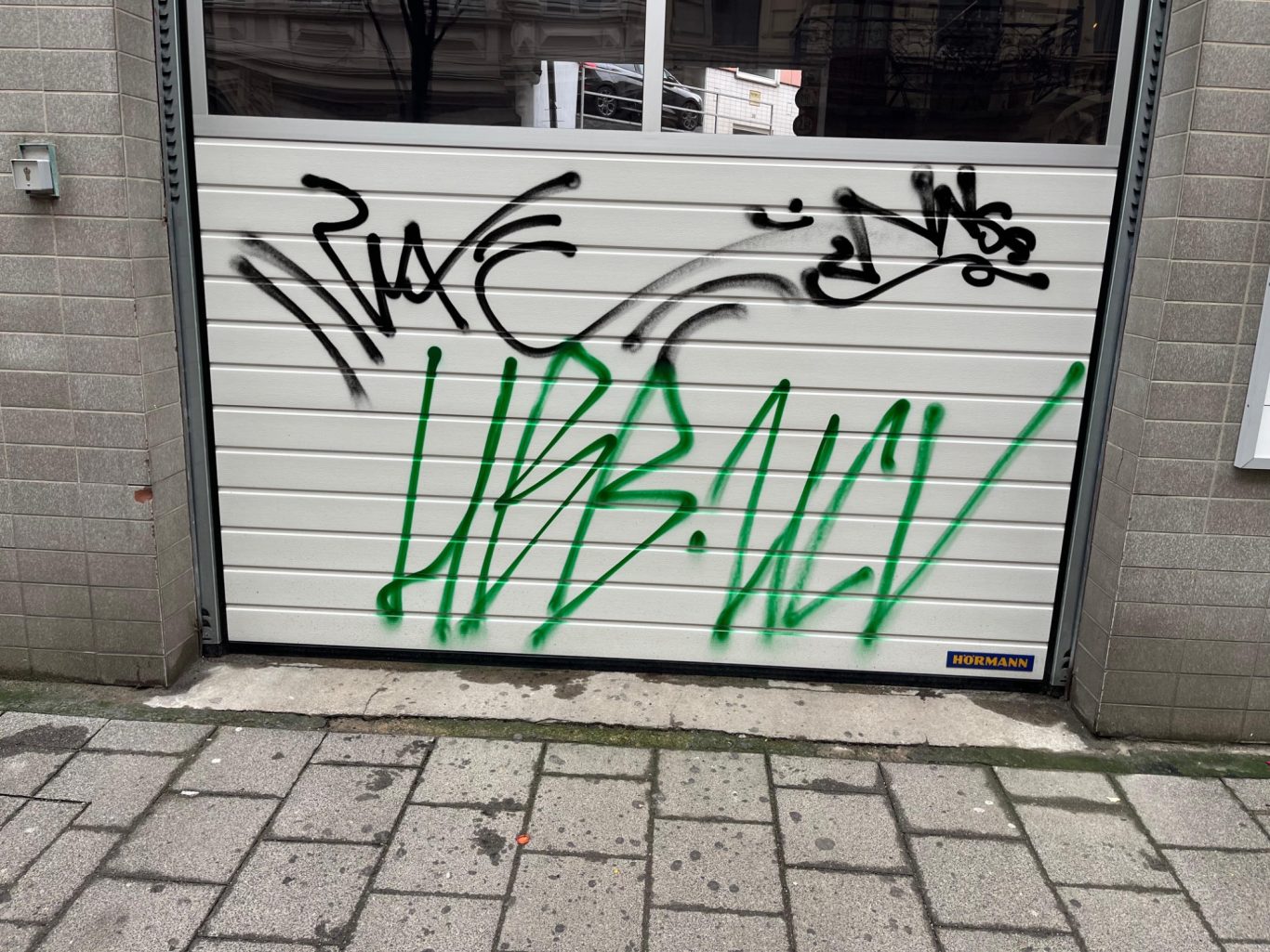 VORHER Graffiti mit schwarzer und grüner Schrift auf einem Rolltor.