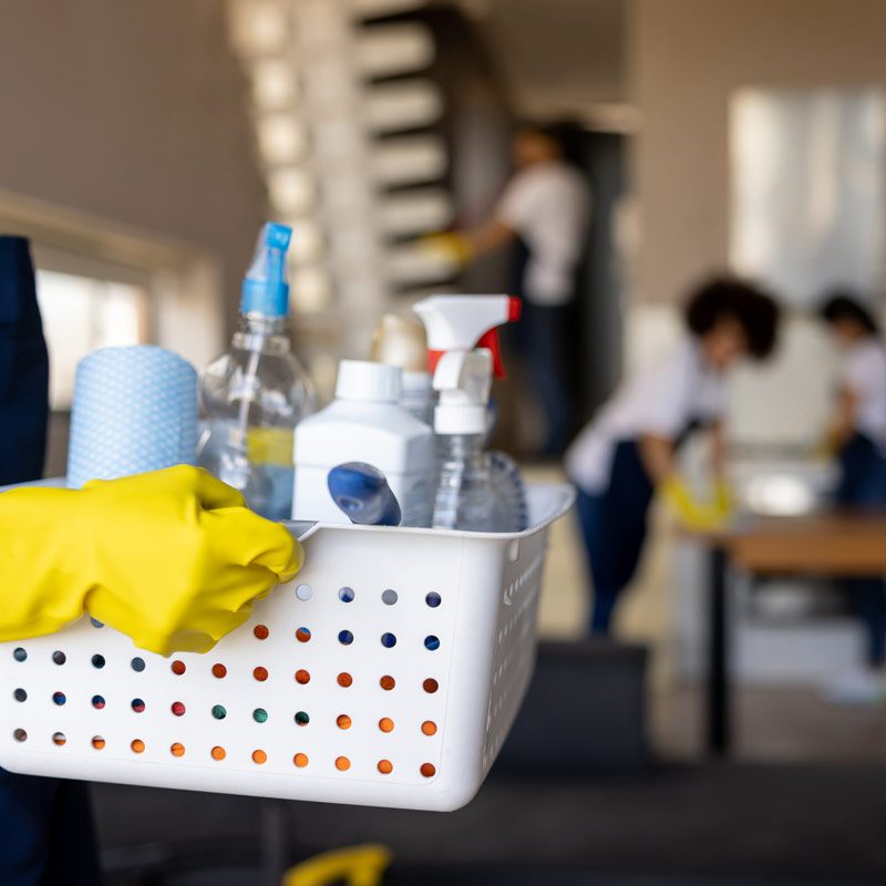 artikelbild unsere geschichte immobilienservice Witting Eine Person mit gelben Handschuhen hält einen Korb mit Reinigungsprodukten.